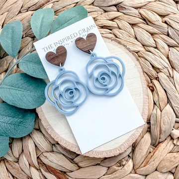 Blue rose earrings on a white card with green leaves on a woven surface