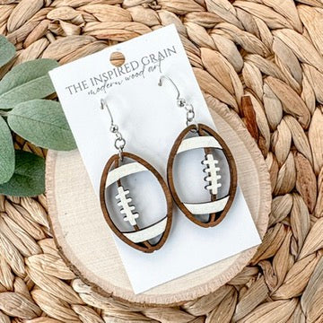 Wooden football-shaped earrings on a 'The Inspired Grain' card with a woven surface background.