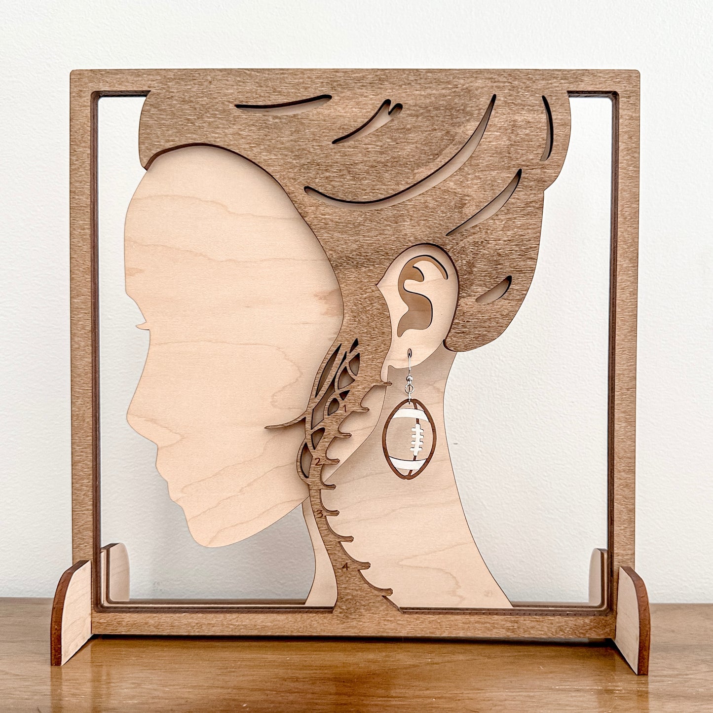 Wooden earring display with a silhouette of a woman's head and an ear, featuring an earring.