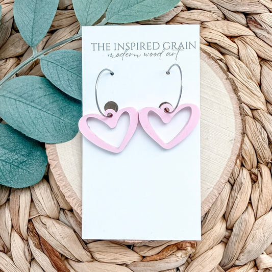 Pink heart-shaped earrings on a 'The Inspired Grain' branded card with leaves in the background