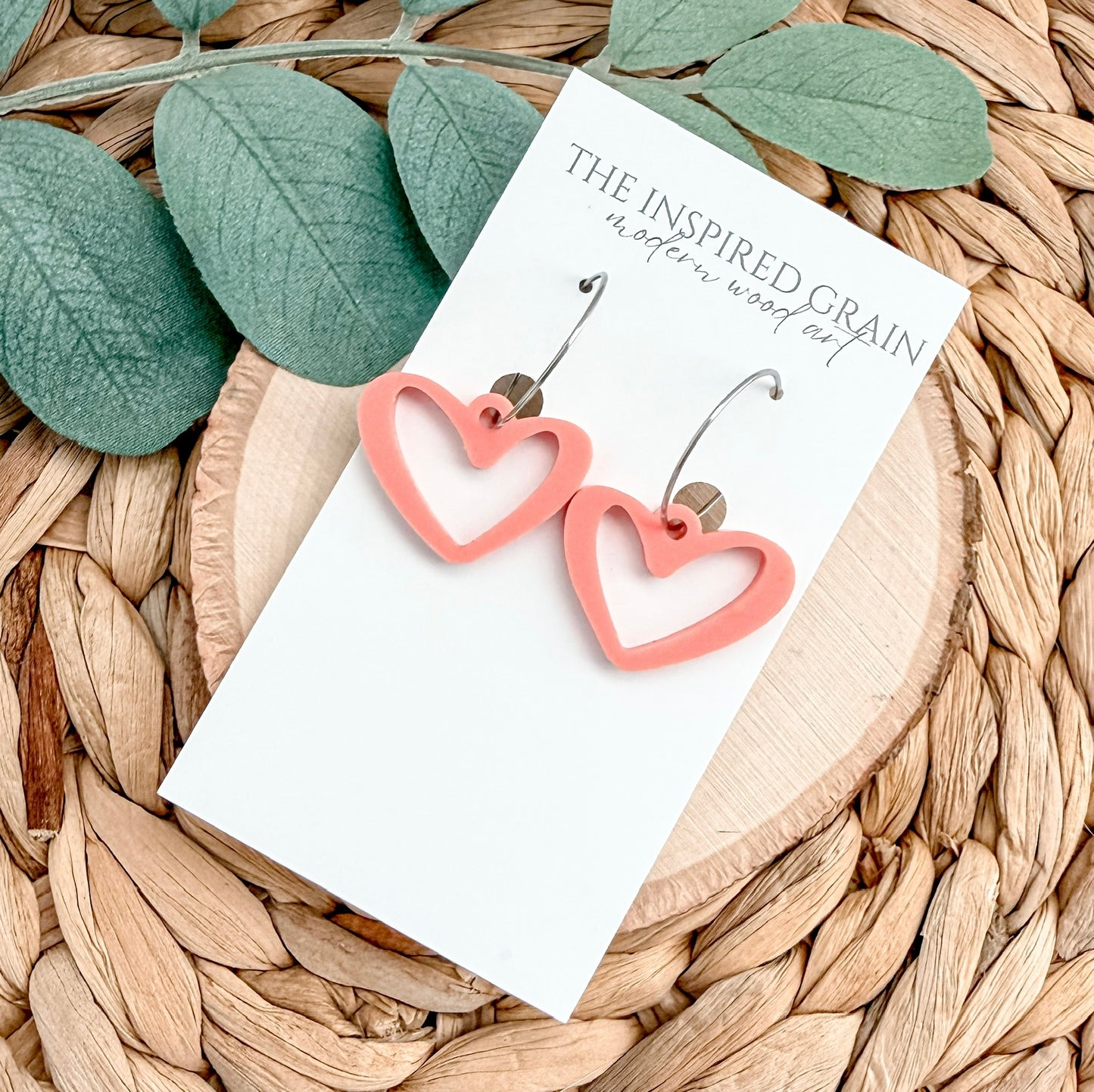 Heart-shaped earrings on a card with green leaves and woven surface