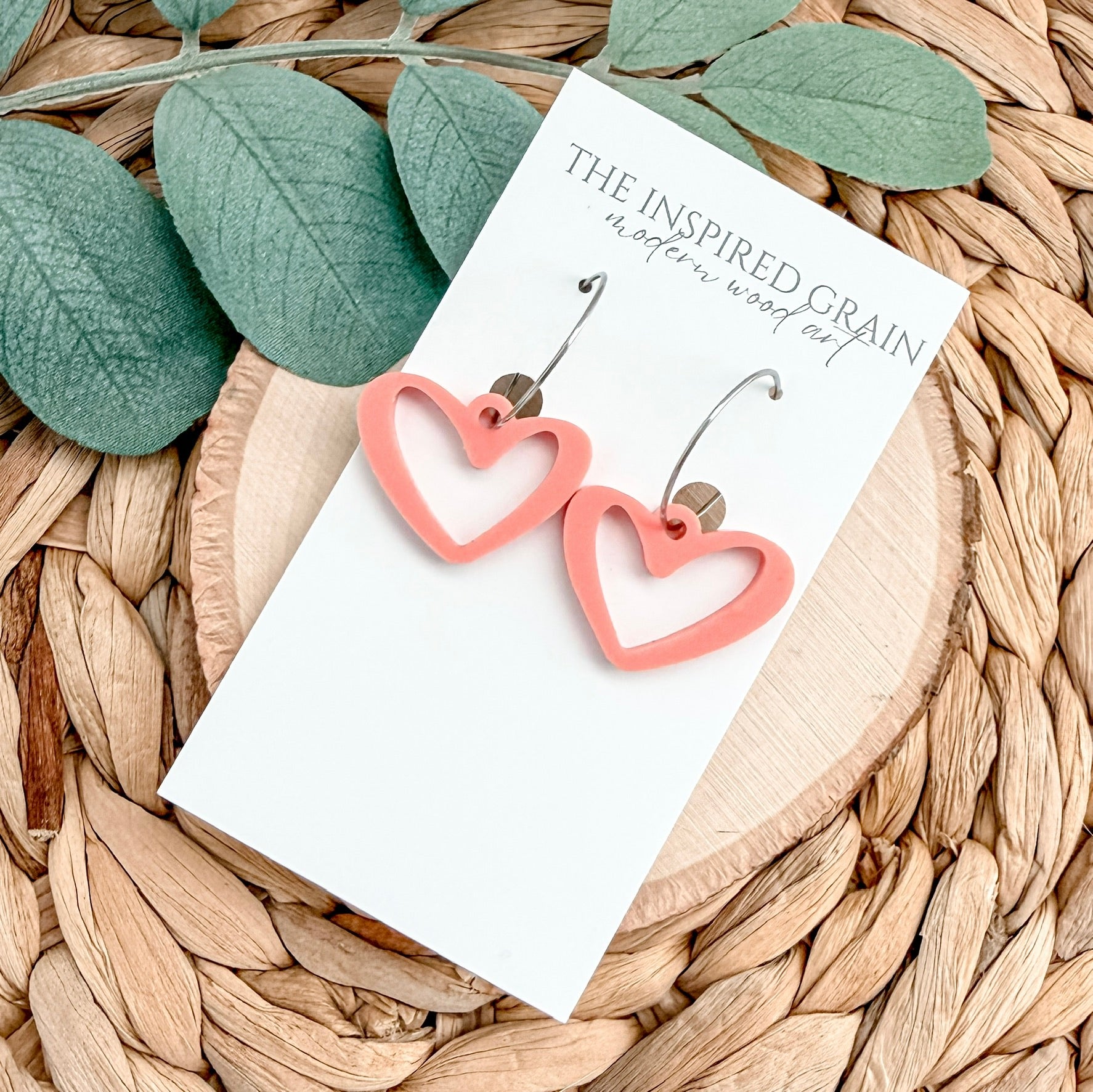 Heart-shaped earrings on a card with green leaves and woven surface