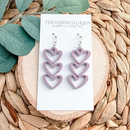 Heart-shaped purple earrings on a 'The Inspired Grain' card with leaves and woven material in the background