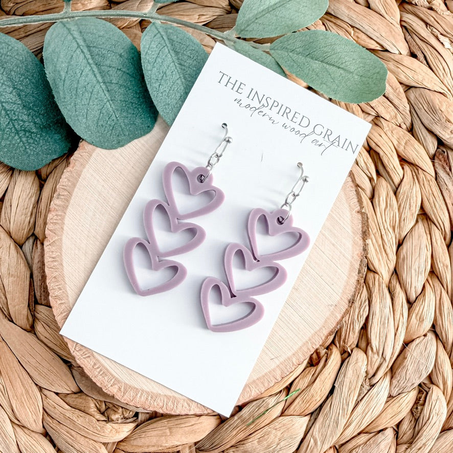 Heart-shaped purple earrings on a card with green leaves and woven surface
