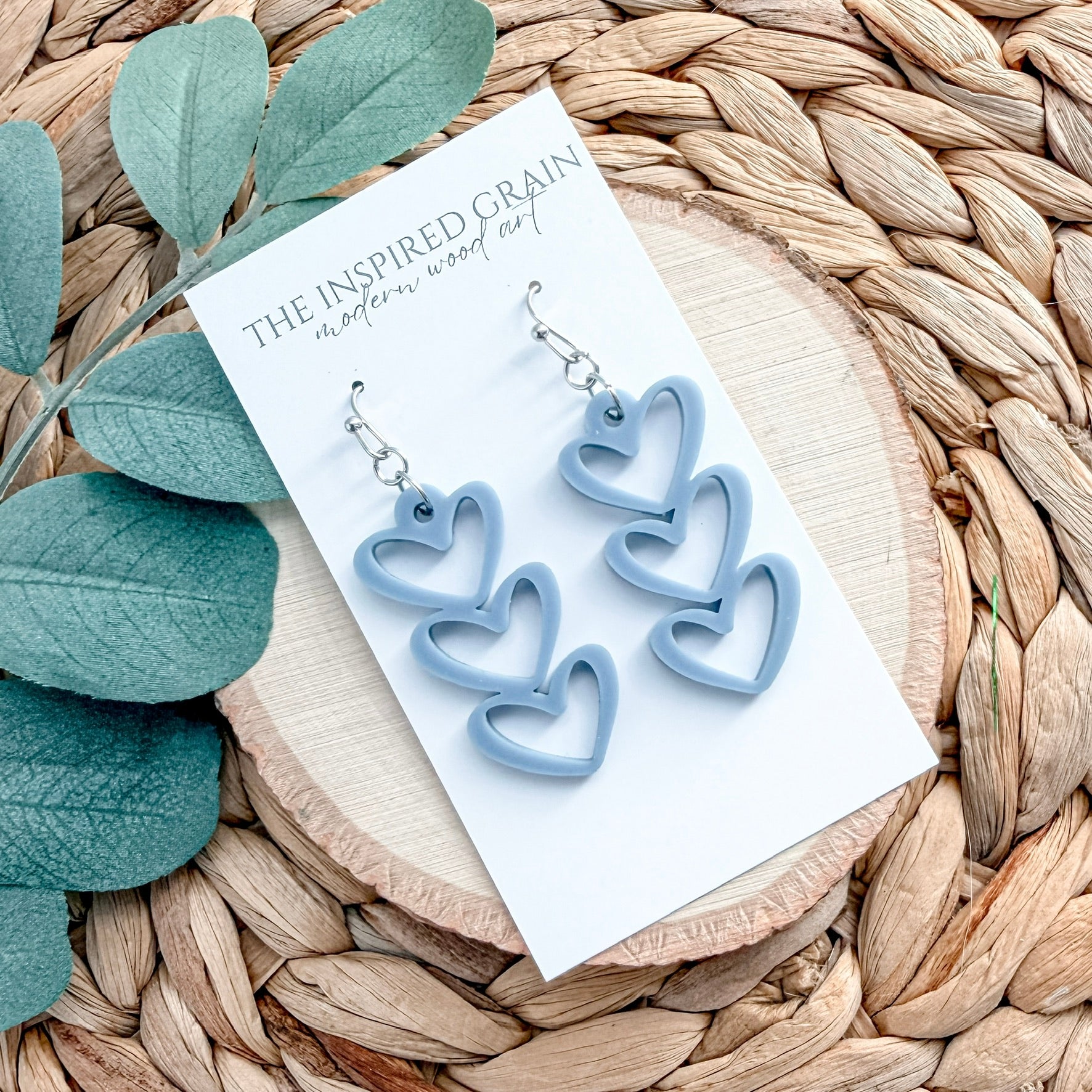 Blue heart-shaped earrings on a branded card with leaves and woven surface