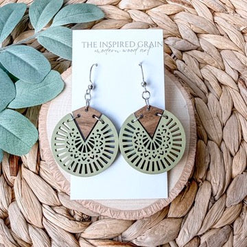 Wooden earrings on a card with 'The Inspired Grain' branding, surrounded by natural elements.
