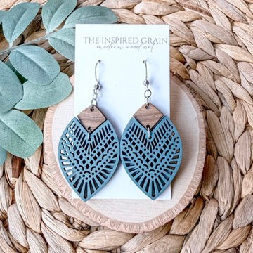 Blue and wooden earrings on a card with 'The Inspired Grain' branding, placed on a woven surface.