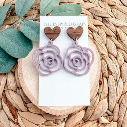 Purple rose-shaped earrings on a 'The Inspired Grain' card with leaves and woven material in the background.