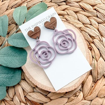 Purple rose-shaped earrings on a white card with green leaves and woven surface