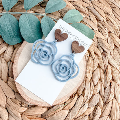 Blue rose earrings on a card with green leaves on a woven surface