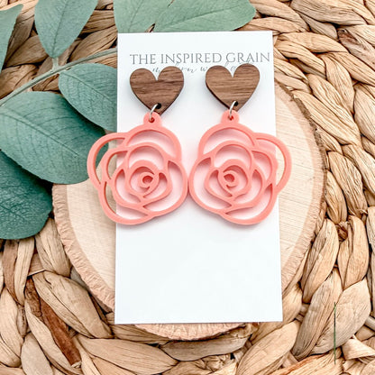 Pink rose-shaped earrings on a white card with 'The Inspired Grain' branding, placed on a woven surface with leaves.