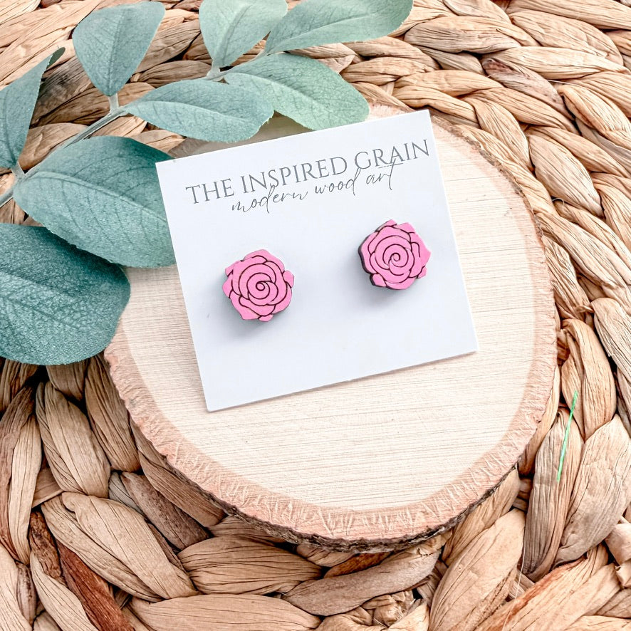 Pink rose-shaped earrings on a 'The Inspired Grain' branded card with leaves and wood background