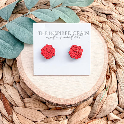 Red rose-shaped earrings on a card labeled 'The Inspired Grain' against a woven background.