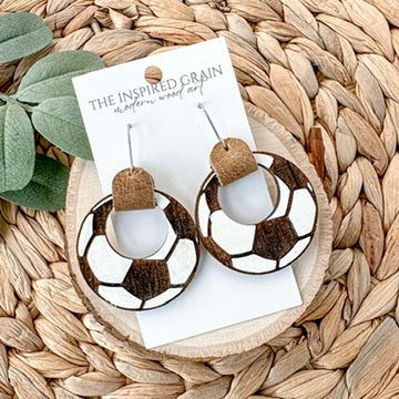 soccer themed hoop earrings on a 'The Inspired Grain' branded card, placed on a woven mat.