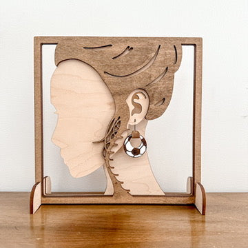 Wooden display stand with a silhouette of a face and an earring on a wooden surface.