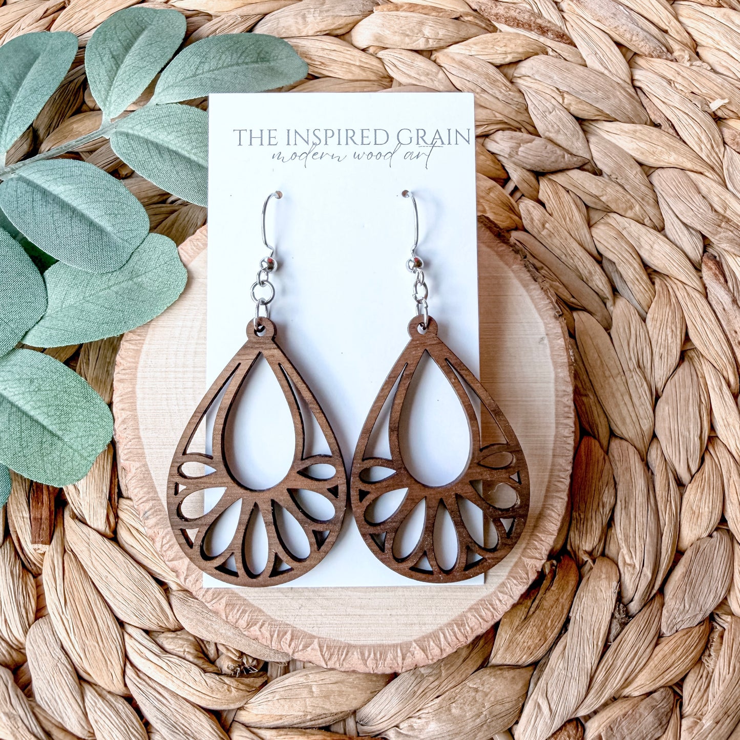 Wooden teardrop earrings on a 'The Inspired Grain' branded card with leaves and woven mat in the background.