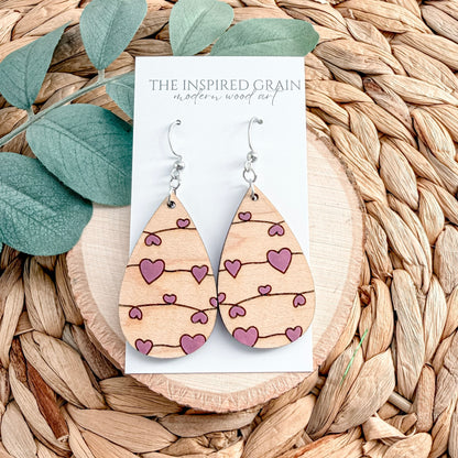 Wooden earrings with heart patterns on a card labeled 'The Inspired Grain' against a woven background.