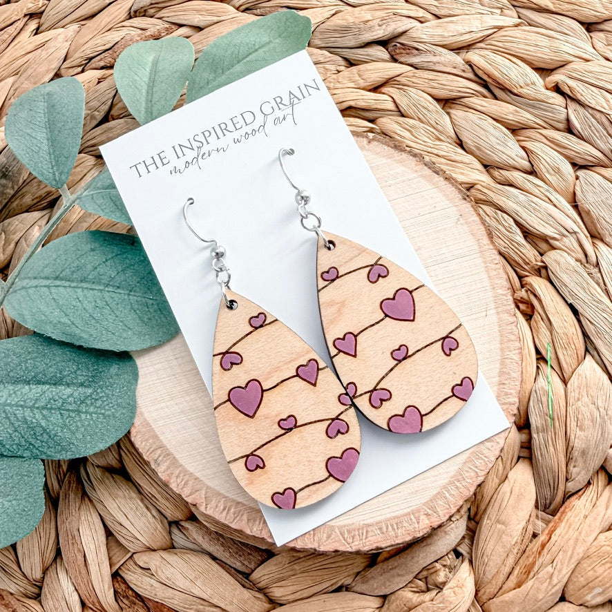 Wooden heart-patterned earrings on a wicker surface with green leaves.