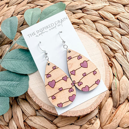 Wooden heart-patterned earrings on a wicker surface with green leaves.