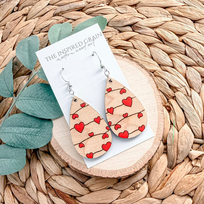 Wooden earrings with red heart patterns on a wicker surface with 'The Inspired Grain' card.