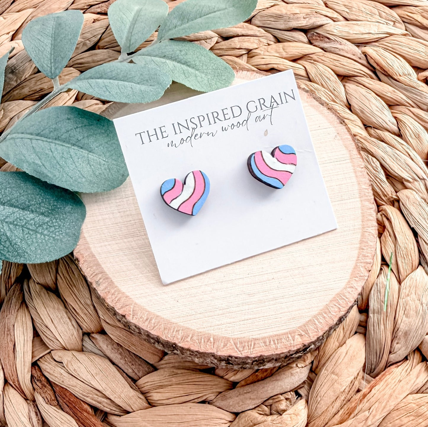Heart-shaped earrings on a 'The Inspired Grain' branded card with leaves and wood slice in the background